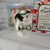 Front view of the cow angel figurine showing detailed painting and design with halo, flower crown, and book.