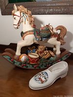 Front view of ceramic rocking horse with colorful saddle and various toys on the rocker base, next to the Villeroy & Boch Christmas shoe.