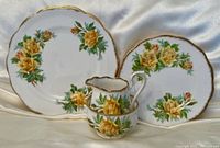 Photo of two plates and a cup with saucer showing yellow rose floral pattern and gold scalloped edges on white china.