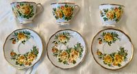 Set of three Royal Albert Tea Rose porcelain tea cups and matching saucers, each decorated with yellow rose floral pattern and gold trim.