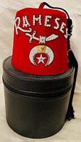 Front view of the red Rameses Shriners fez placed on top of the black carrying case showing decorative sequins and symbols.