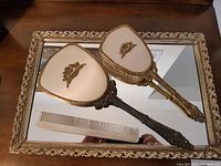 Overview of the glass tray with ornate gold-toned frame and the hand mirror, brush, and comb placed on top