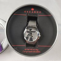 Close-up image of the Oscardo INUKSHUK watch inside the round metal case with branding visible on the interior.