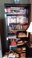 Full view of the wood bookcase filled with various books, DVDs, and media items, showing its six shelves and dark wood finish.