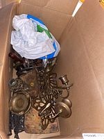 View inside a cardboard box showing various brass candle holders, ashtray and drawer handles scattered inside