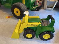 Front and side view of green and yellow John Deere child's ride-on toy tractor with a front loader bucket and four black plastic tires with yellow centers.