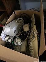 Box of computer parts containing beige keyboards, mice with ball sensors, speakers, multiple cables, and a telephone handset.