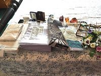 Lot arrangement on floral tablecloth showing sheets, boxed sheet set, shower curtain liner, water bottle cover, small wall decor, and five perfume bottles