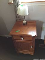 Full view of vintage wood nightstand with small table lamp on top, showing size, color, and condition.