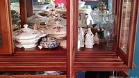 Photo of cabinet interior showing ceramic serving bowls with floral designs, figurines, and salt and pepper shakers.