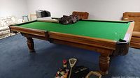 Corner view of oak pool table with green felt and assorted accessories on top