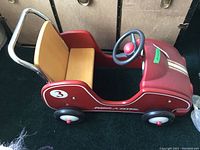 Left side view of the vintage Radio Flyer ride-on car, showing red metal body, wooden seat, and number 3 decal on the side.