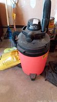Front view of the Shop-Vac wet/dry vacuum showing the red tank base, black lid, and flexible hose attached.