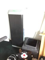 Ultimate Fitness adjustable step platform with four risers shown against a wall on a black carpeted floor, with a plush toy partially visible nearby.