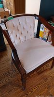 Side angle of the vintage wooden chair showing the curved armrest, tufted upholstered back and seat, and wood frame.