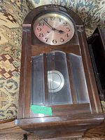 Full view of the wooden wall clock showing the glass front door, carved top, and pendulum inside.