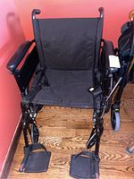 Front view of the black Cruiser X4 collapsible wheelchair showing fabric seat, footrests, armrests, and push handles.