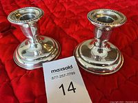 Pair of Birks silver candle holders displayed on a red fabric background, showing the top and side view.