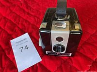 Front view of the Brownie Hawkeye box camera showing lens, viewing window, and leather strap.