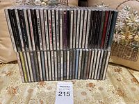 Full view of approximately 40 music CDs arranged in two rows on a floral fabric background with pillows behind.