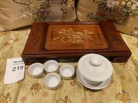 Wide view of closed wooden tea tray with ceramic gaiwan and four cups arranged in front