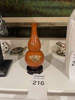 Orange glazed double-gourd shaped decorative vase with gold and white floral patterns on black round stand.