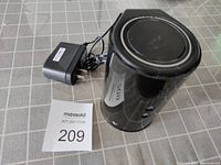 Top and side angle photo of black cylindrical D-Link DIR-818L router with power adapter beside it on a grey grid surface.