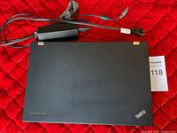 Closed Lenovo ThinkPad laptop with charger visible, placed on a red surface.