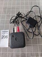 Top view of black Logitech Bluetooth wireless speaker adapter with cables and power supply on grid surface.