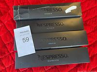 Four black boxes of Nespresso coffee capsules labeled Stormio, Altissio, Odacio, and Diavolitto on a red quilted surface.
