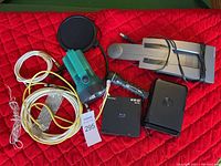 Top-down photo of assorted cables, pop filter, microphone, headphones, Blu-ray player, and a black external device on red quilted surface