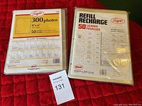 Two packs of Snap'n branded photo storage sheets on a red surface, one pack for 300 photos (50 sheets) and one refill pack with 50 sheets