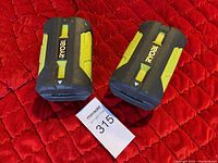 Two Ryobi branded lithium-ion power tool batteries placed upright showing front with brand logo and yellow detail.