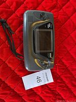 Black Sega Game Gear portable handheld game console on a red quilted background with MaxSold lot card visible