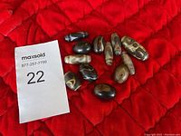 Eleven Dzi beads displayed on red quilted fabric next to MaxSold lot number card