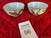 Pair of vintage Chinese bowls on red fabric, showing exterior colorful dragon and floral designs with gold rims.