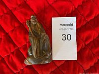 Front view of the carved buffalo horn sculpture seated figure next to identification card.