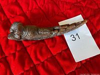 View of the left side of the carved buffalo horn sculpture on a red quilted background, showing detailed carving of the buffalo's head and body.