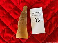 Side view of the buffalo horn sculpture showing shape, texture, and carved detail with a red background and MaxSold number tag.