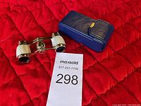 Vintage opera binoculars with white inlay and blue leather case placed on red quilted fabric.