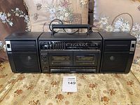 Front view of the vintage Sony boombox with dual cassette player and detachable speakers on each side, placed on a patterned fabric surface with pillows in the background.