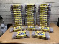 Front view of 38 sets of Bandaloom craft kits stacked and laid out on a table, each kit in a plastic case with yellow label showing children with colorful bands.