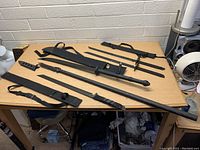 Top down view of 5 black tactical swords arranged on a table with sheaths and carrying straps.