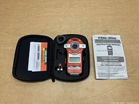 Top view of closed carrying case open, showing laser level device, small mounting accessory, instruction manual, and warranty card inside.
