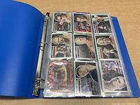 Blue three-ring binder open with plastic sleeves displaying a grid of WWE wrestling cards featuring wrestlers like Hulk Hogan.
