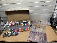 Large assortment of beads in several plastic containers and small jars inside an open cardboard box