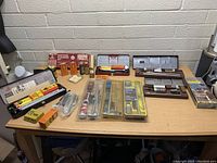 Wide angle image showing multiple firearm cleaning kits and accessories arranged on a wooden work table