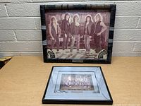 Two framed pictures of Flotsam & Jetsam on a table against a white brick wall.