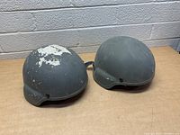 Two MSA military-style helmets on a table showing overall shape and paint wear.