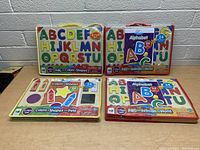 Four LeapFrog Lift & Learn Playsets arranged on a table, showing front of cases with alphabet letters and various shapes visible.